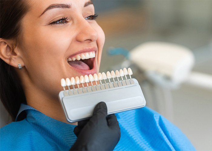 A smiling patient holding a tooth shade guide, illustrating teeth whitening or veneer options